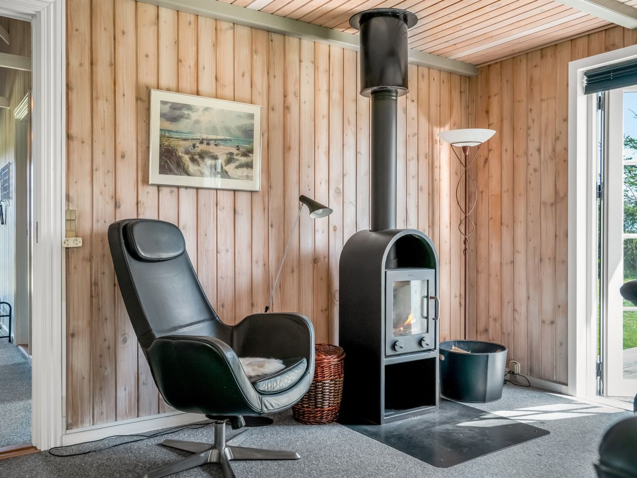 Une pièce moderne avec des murs lambrés, un fauteuil noir, une cheminée et une fenêtre.