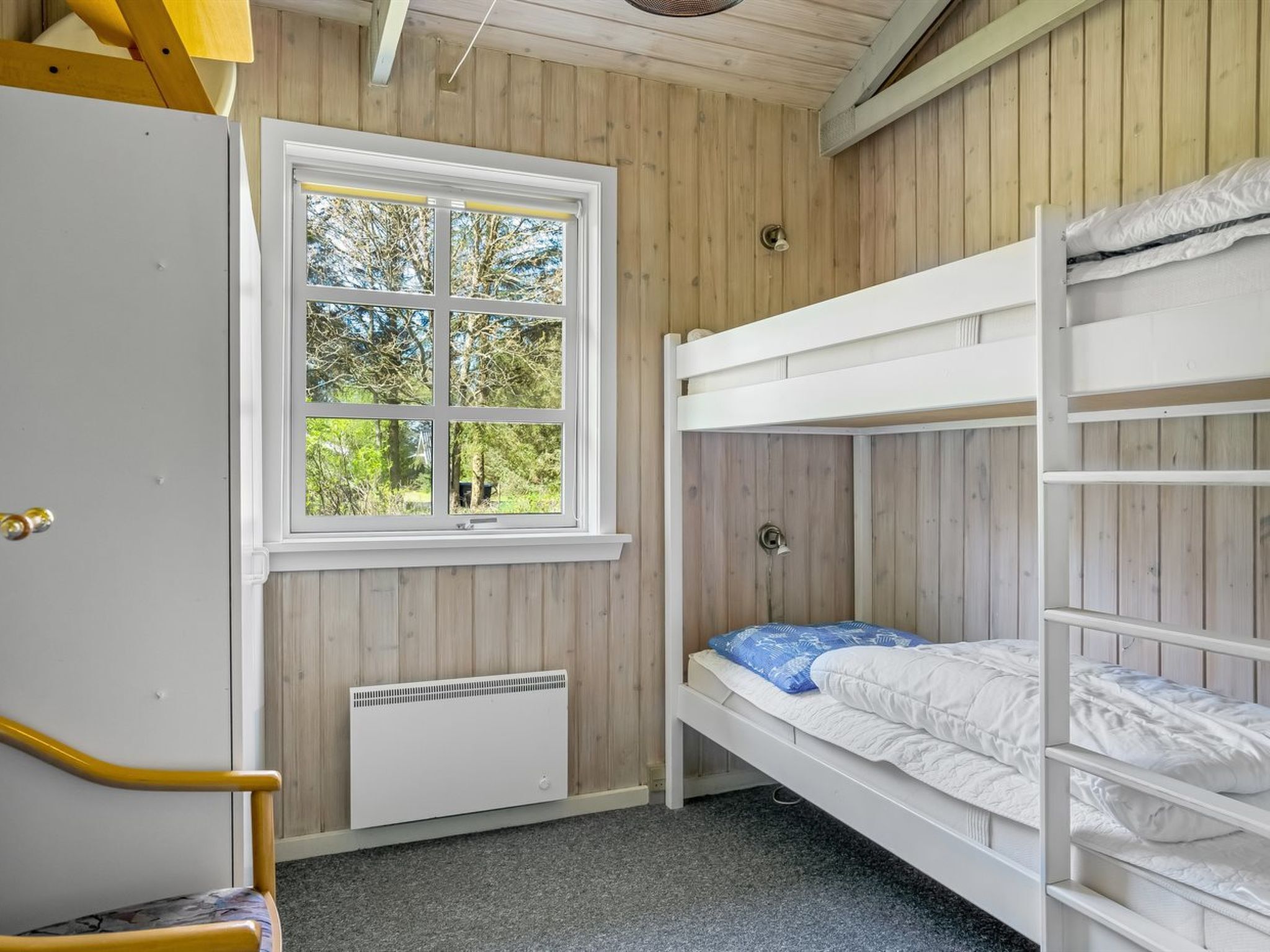 A bunk bed room with a window, a radiator, and a door.