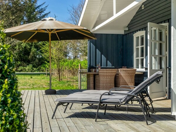 Une terrasse extérieure avec deux chaises longues et un grand parasol, une table en osier et un barbecue.
