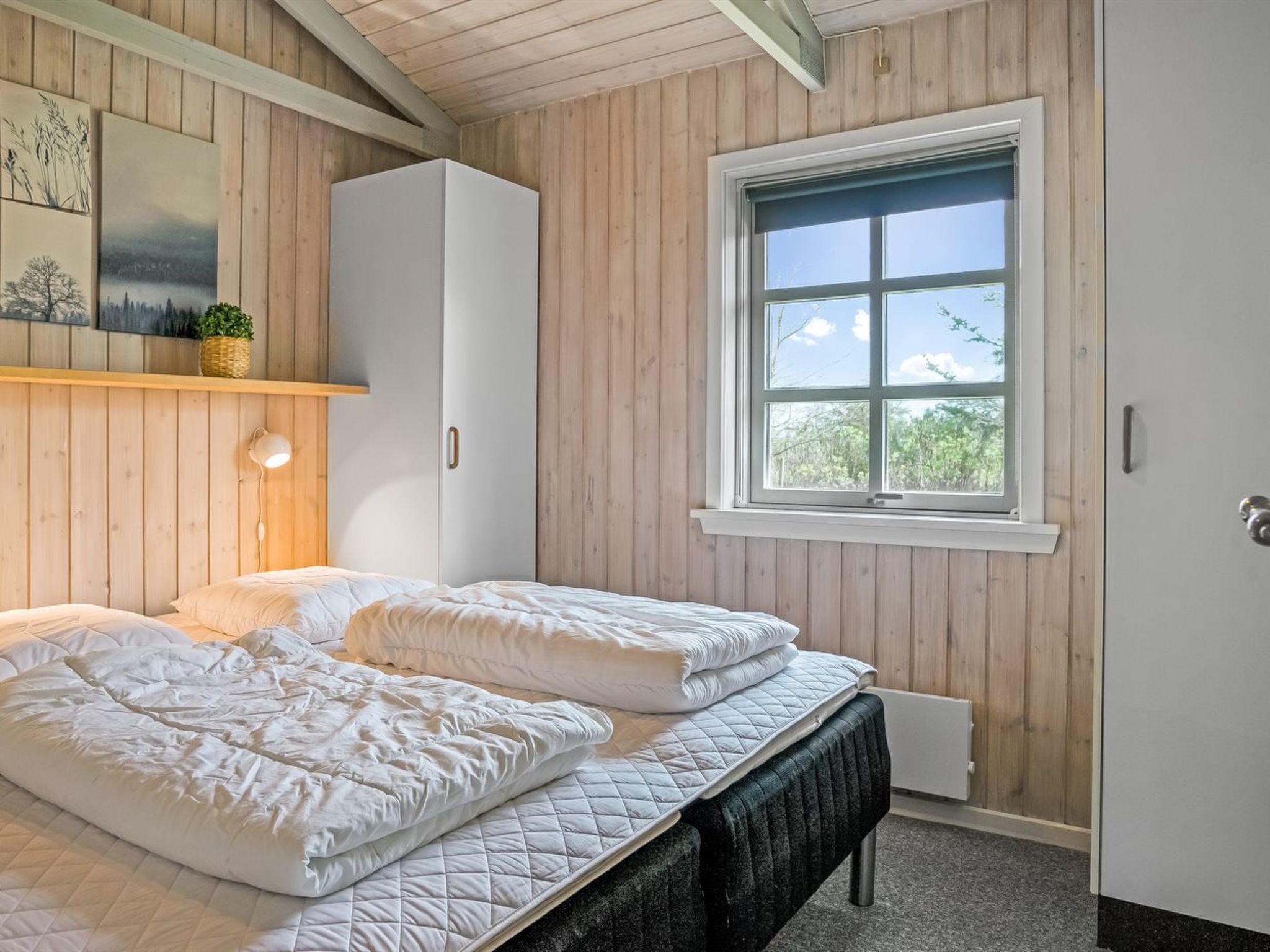 Une chambre à coucher avec un lit, une fenêtre, des murs en bois et une armoire blanche.