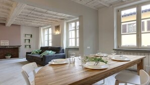 Uma sala de jantar com uma mesa de madeira posta para quatro, um sofá e uma lareira.