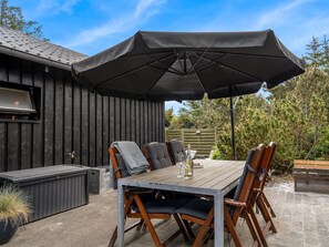 Un espace extérieur aménagé pour les repas, avec une table, des chaises et un grand parasol.