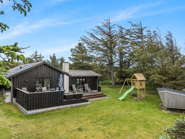 Une cabane en bois avec une terrasse, une maisonnette et un toboggan.