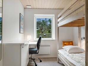 Une chambre avec un lit superposé, un bureau avec une chaise, un radiateur et une fenêtre donnant sur des arbres.