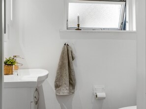 Une salle de bain avec un lavabo blanc, un porte-serviettes avec une serviette, une fenêtre avec une bougie et un porte-rouleau de papier toilette.