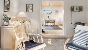 Ein Zimmer mit Holzboden, einer Essecke mit Tisch und Stühlen, einem Sofa mit gestreiftem Kissen und einem an der Wand befestigten Lautsprecher.