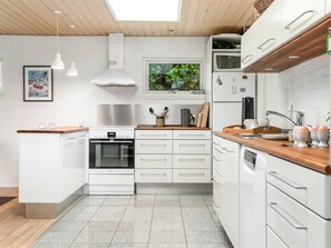 Eine moderne Küche mit weißen Schränken, einem Backofen, einer Mikrowelle und einem Fenster mit Blick auf Grünflächen.