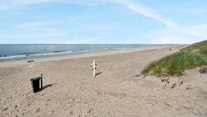 Une plage avec une bouée de sauvetage, une poubelle et des dunes herbeuses.