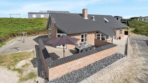 Une maison moderne avec un toit en pente, un patio doté de mobilier d’extérieur et une vue sur le paysage environnant.