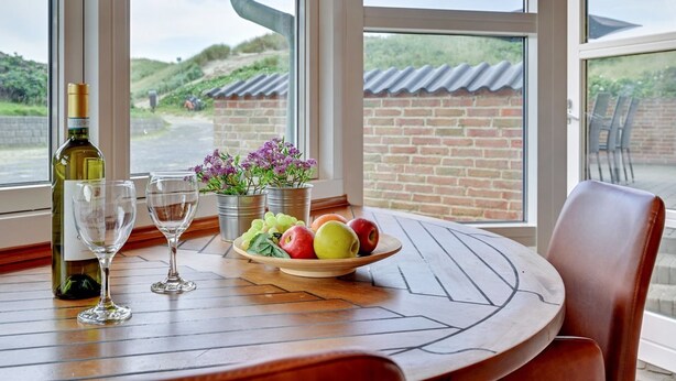 Un coin repas avec une table dressée pour deux personnes, agrémenté d’une bouteille de vin, de verres, d’un saladier de fruits et de plantes en pot.