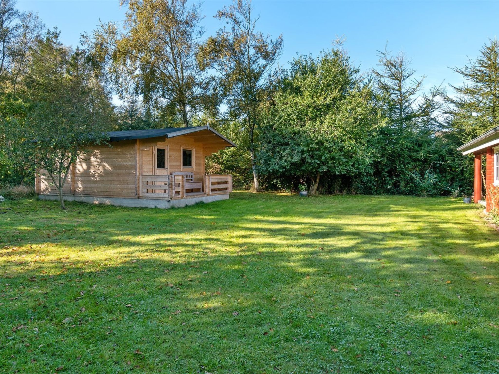 Une petite cabane en bois dotée d’un porche, entourée d’une pelouse bien entretenue et d’arbres touffus.
