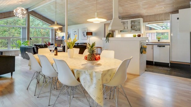 Une cuisine moderne avec des meubles blancs, un grand îlot central et un coin repas comprenant une table ronde et des chaises.