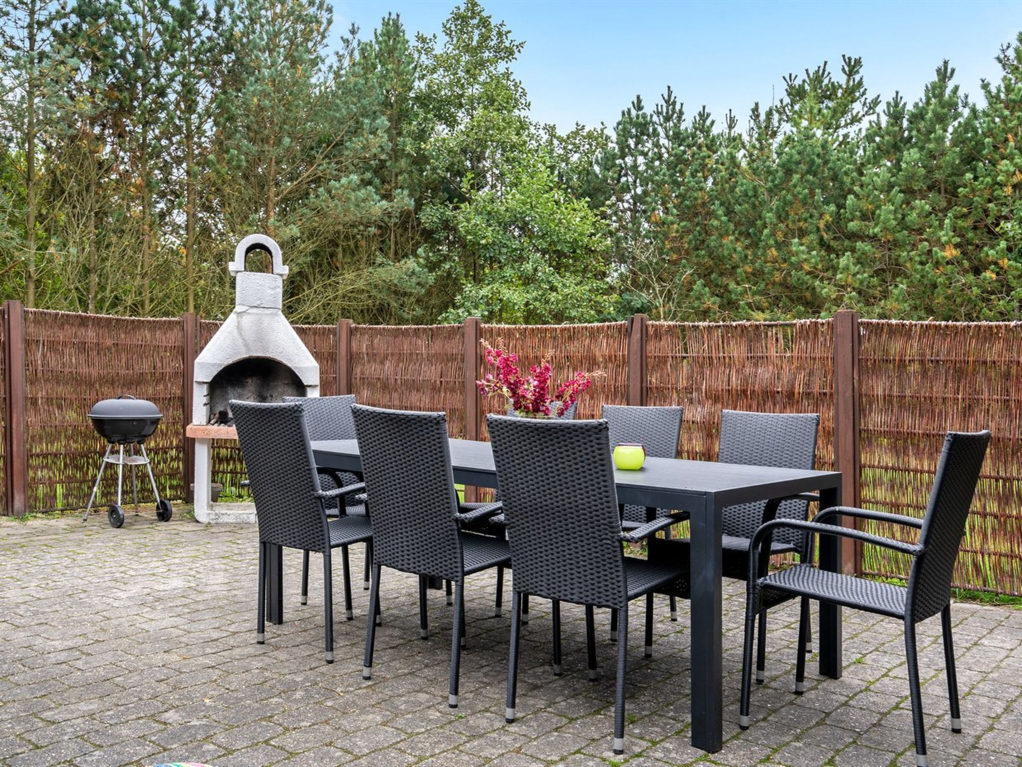 An outdoor patio with a stone-tiled floor, a table with chairs, a barbecue grill, and a stone oven.