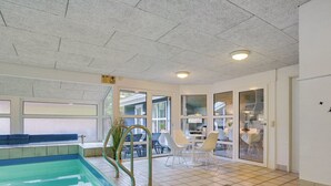 Une piscine avec un jacuzzi, des portes vitrées donnant sur un coin repas et un espace salon offrant une vue sur l’extérieur.