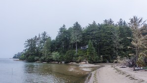 Ein Strand mit sandigem Ufer, dichtem Wald und einem Haus, das teilweise von Bäumen verdeckt wird.