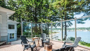 Eine Terrasse mit Sitzgelegenheiten im Freien, einer Feuerstelle und Blick auf ein Gewässer.