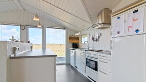 A modern kitchen with white cabinetry, a stainless steel range hood, and a refrigerator with magnets.