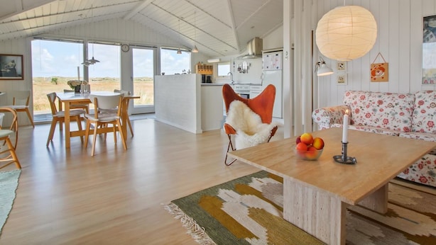A spacious living area with a wooden dining table, a sofa with floral upholstery, and a large window offering a view of the outdoors.