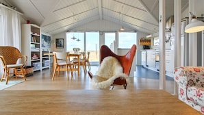 A spacious living area with a high ceiling, a dining table, and a cozy armchair.