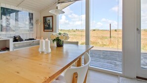 A spacious room with a wooden dining table, white chairs, a laptop, and a vase of flowers.