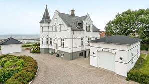 Une grande maison blanche à deux étages, dotée d’un toit à forte pente et d’une tour imposante.