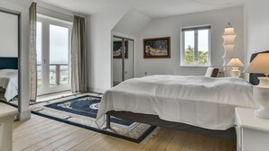 Une chambre avec un grand lit, une fenêtre, un tableau et une vue sur l’extérieur.