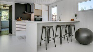 A modern kitchen with white cabinetry, a central island with stools, a large exercise ball, and a window with a view of trees. - "Sighwith" - 500m from the sea by Interhome (Hals)