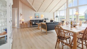 Spazioso loft con soffitto alto, travi in legno, zona pranzo con tavolo e sedie, divano e angolo cottura con finestra vista su un paesaggio verde.