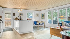 A modern kitchen with white cabinetry, a central island, and a dining area with blue chairs. - "Milan" - 250m to the fjord by Interhome (Thyholm)