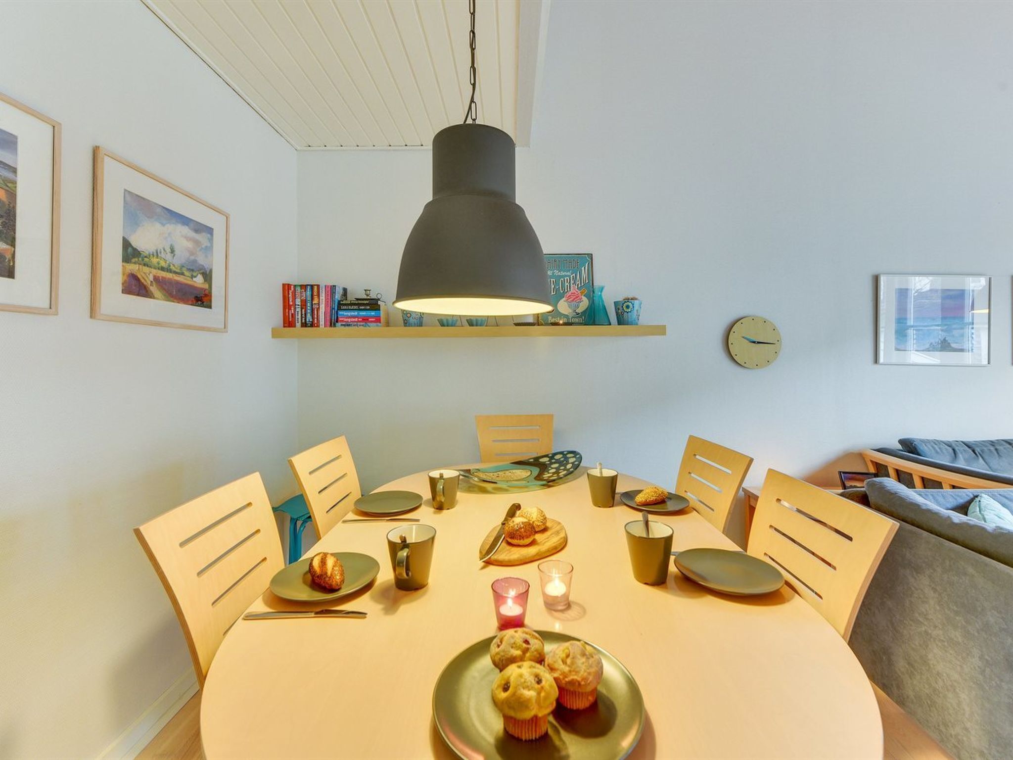 En matplats med ett runt bord, stolar, en hängande lampa, en klocka och en bokhylla med böcker och dekorativa föremål.