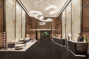 Een hotel lobby met een receptiebalie, een zithoek en een decoratief plafond.