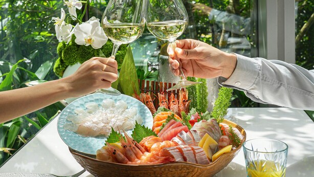 Ein Esstisch mit Meeresfrüchtegerichten, einem Glas Weißwein und Blick auf Grünflächen.