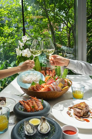 Une table à manger dressée avec des plats de fruits de mer, un verre de vin blanc et une vue sur la verdure environnante.