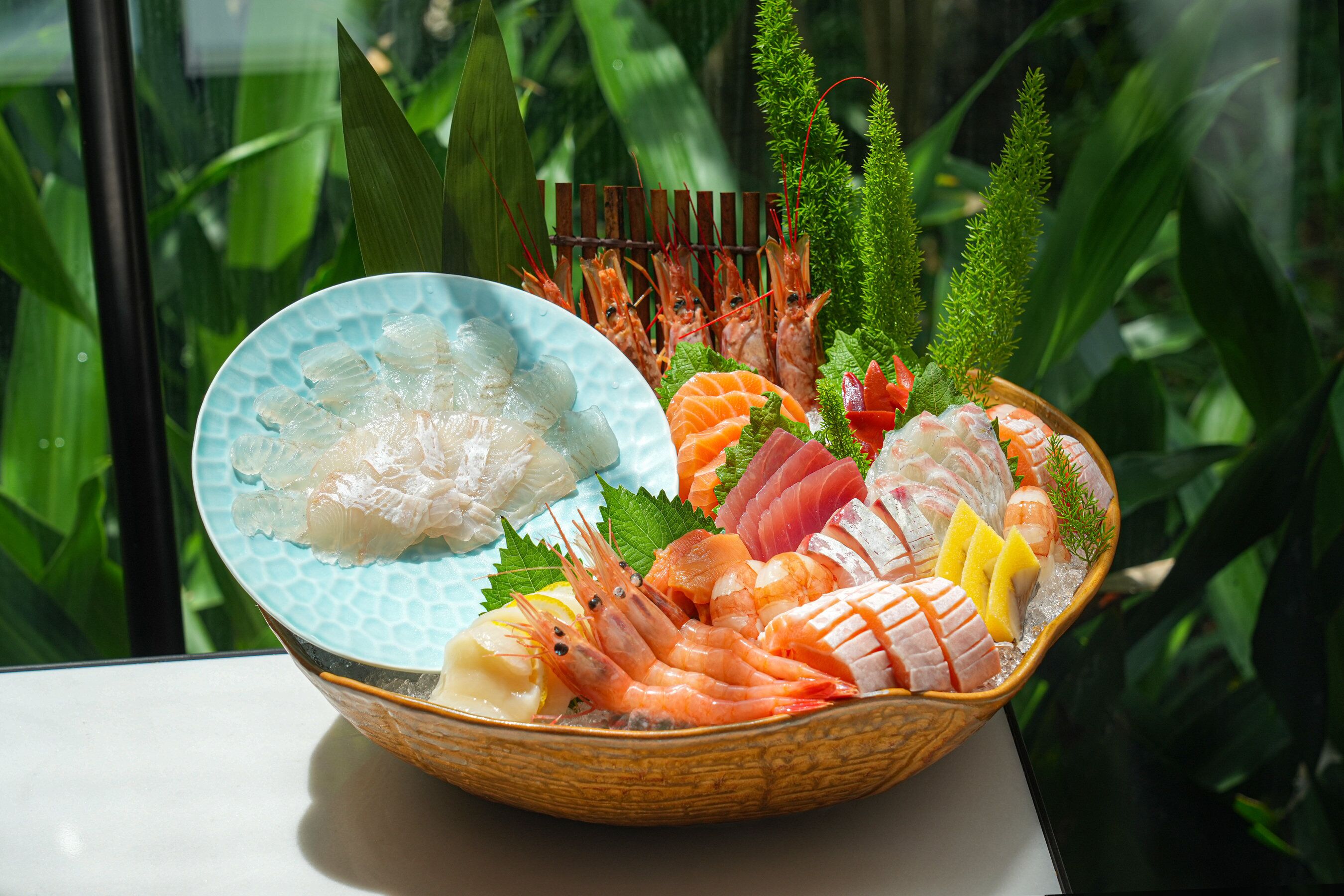 A seafood platter with various types of fish and shrimp, garnished with herbs and lemon slices, presented on a woven basket.