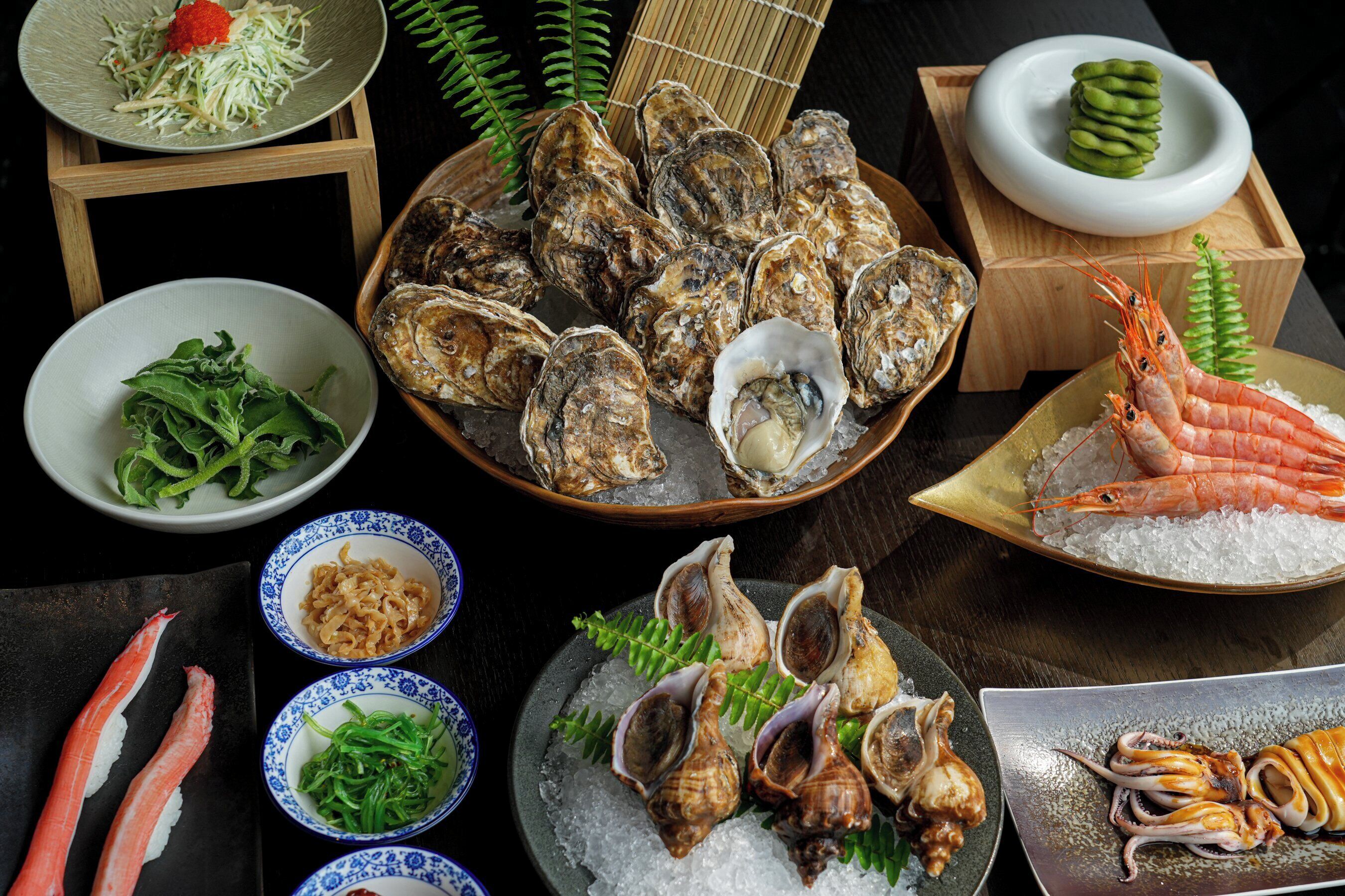 A variety of seafood dishes, including oysters, shrimp, and squid, arranged on a table.