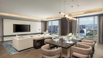 Una habitación de hotel moderna con una televisión de pantalla plana grande, un sofá, una mesa de comedor con sillas y vistas a la ciudad.