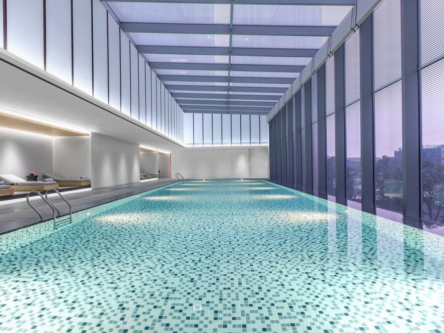Une piscine intérieure avec un sol carrelé, un plafond en verre et une vue sur la ville.