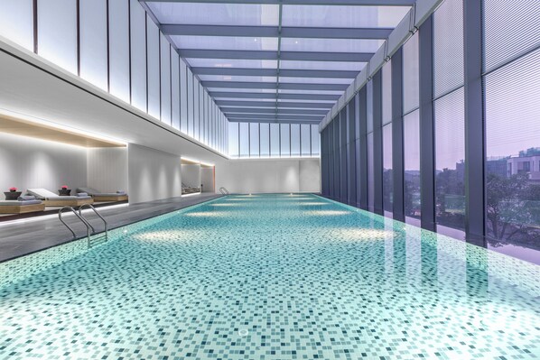An indoor swimming pool with a tiled floor, a glass ceiling, and a view of the city.