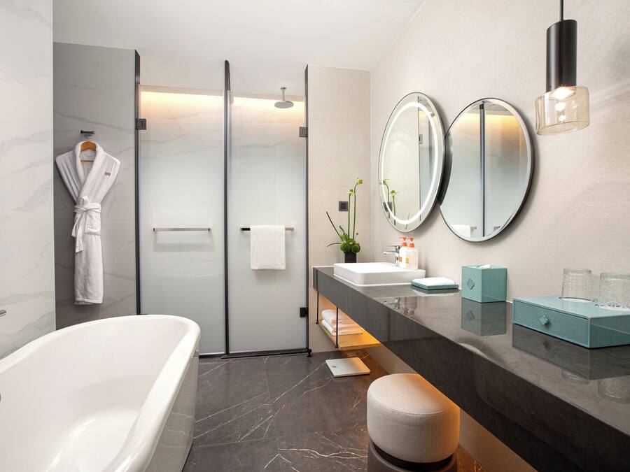 A modern bathroom with a bathtub, glass shower enclosure, dual mirrors, and a vanity with a sink and towel rack.