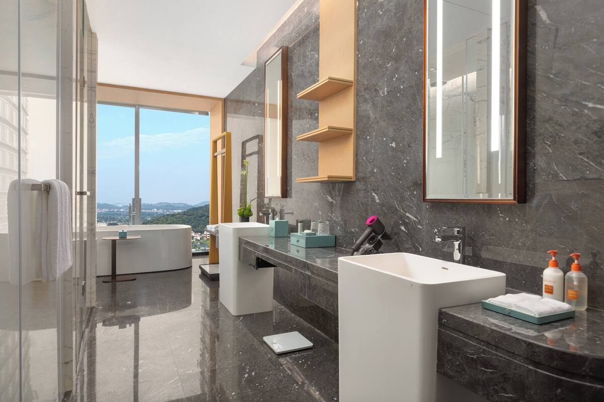 Une salle de bain moderne avec deux lavabos, un grand miroir et une vue sur la ville.