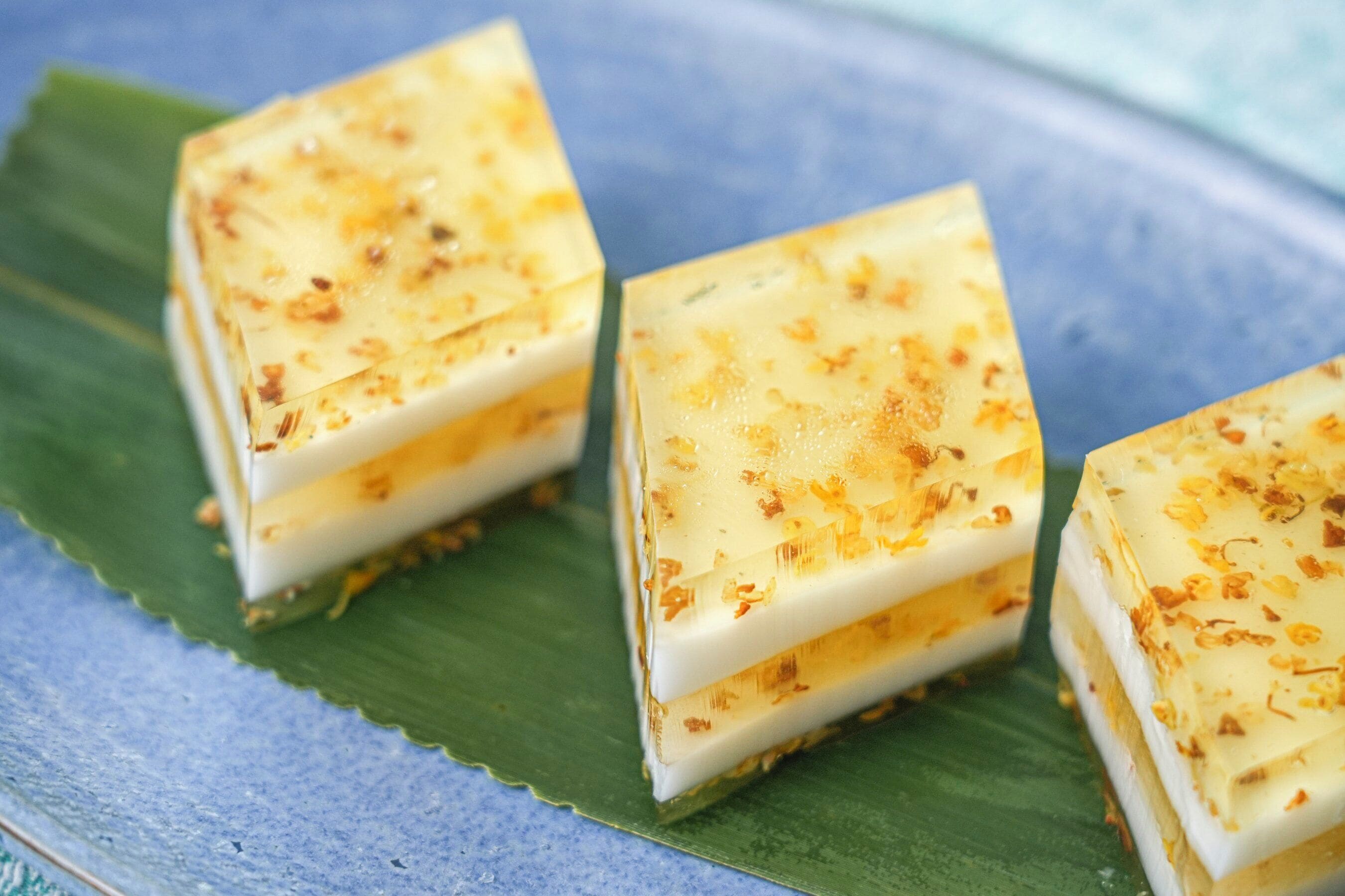 Three square-shaped desserts on a blue plate with a green leaf underneath.