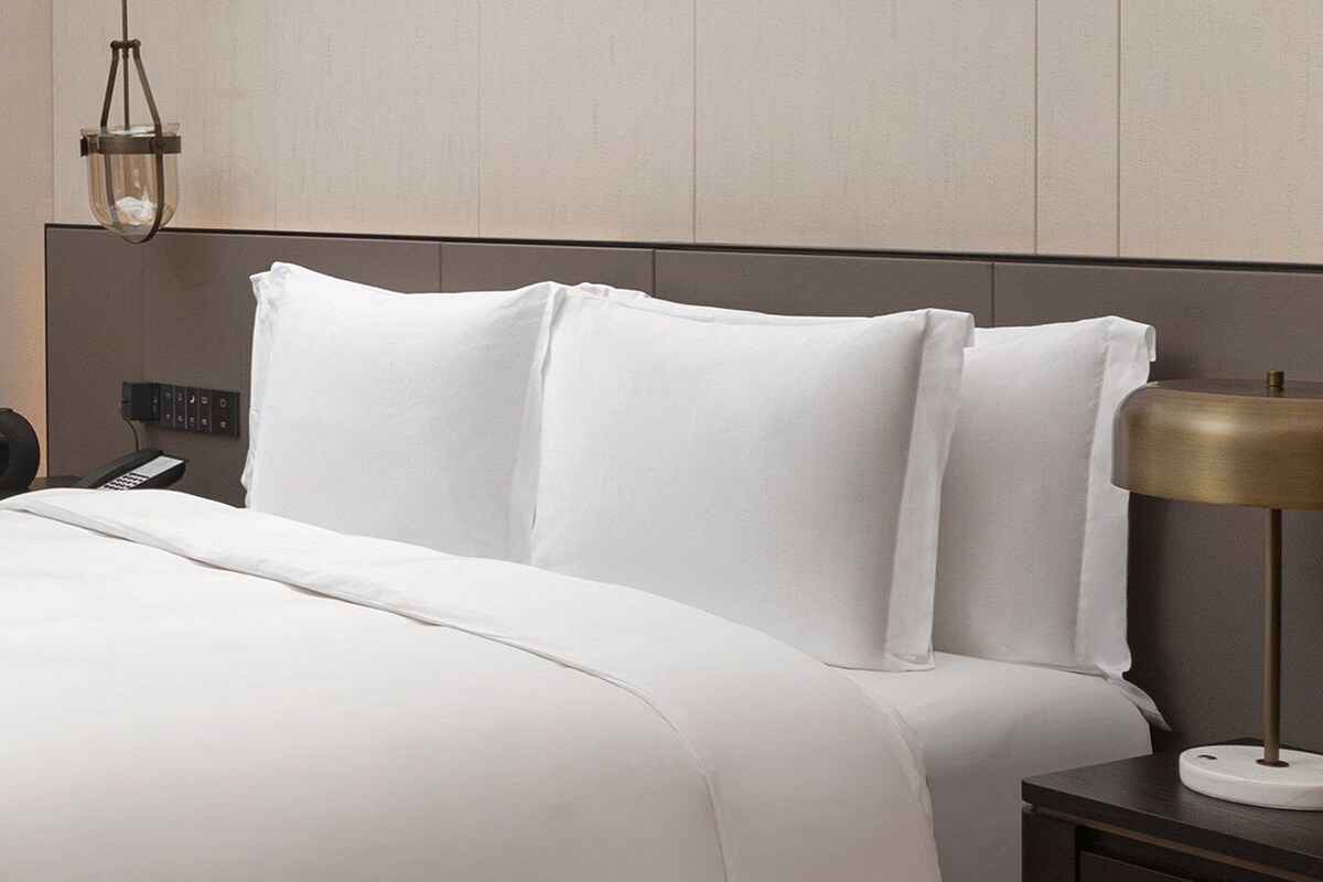 Een hotelkamer met een bed, nachtkastje, lamp, telefoon en bedieningselementen aan de muur.