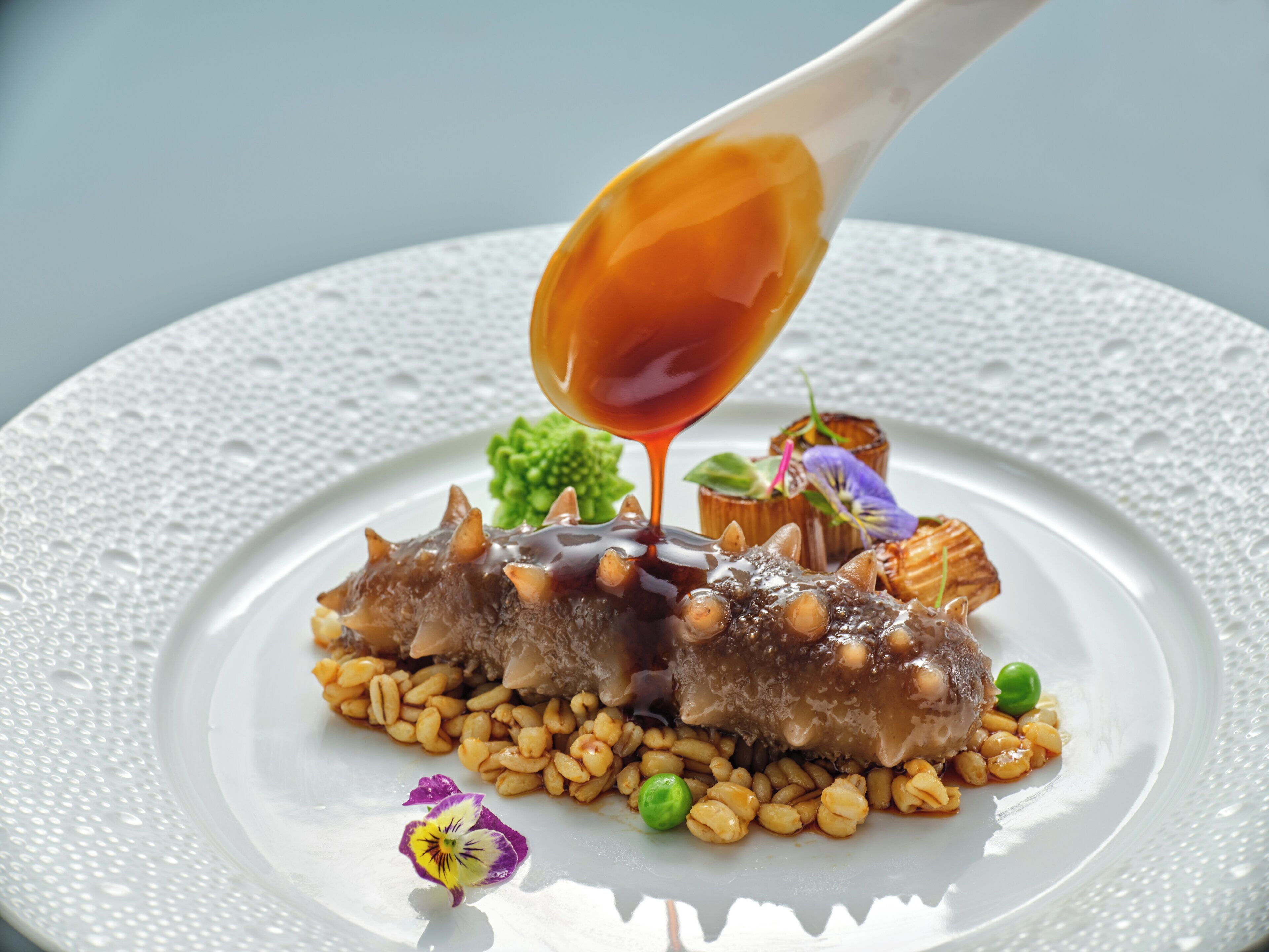 A white plate with a dish of food, including what appears to be a meat dish with beans and garnishes.