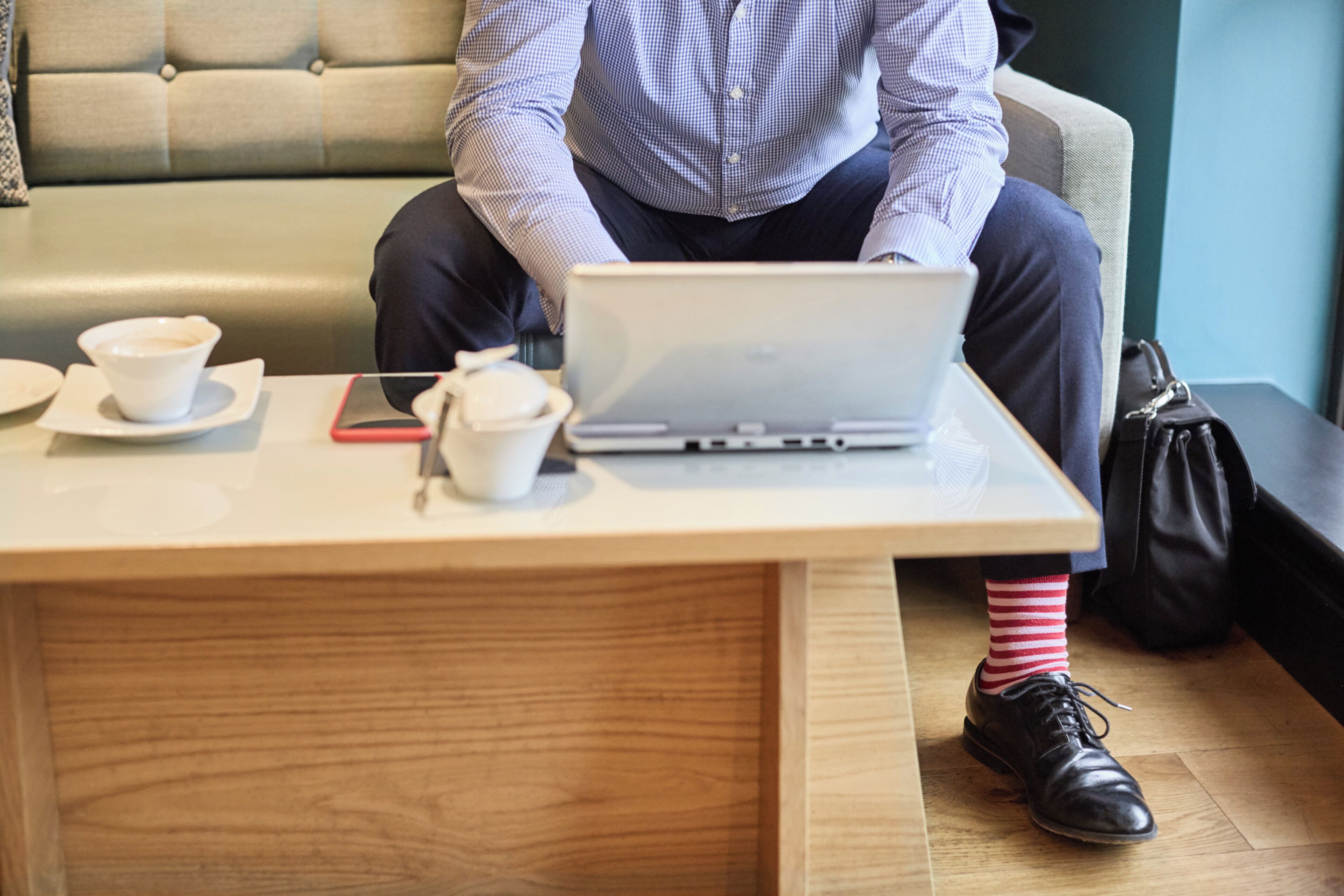A person sitting on a couch with a laptop, a cup, and a smartphone on a table.