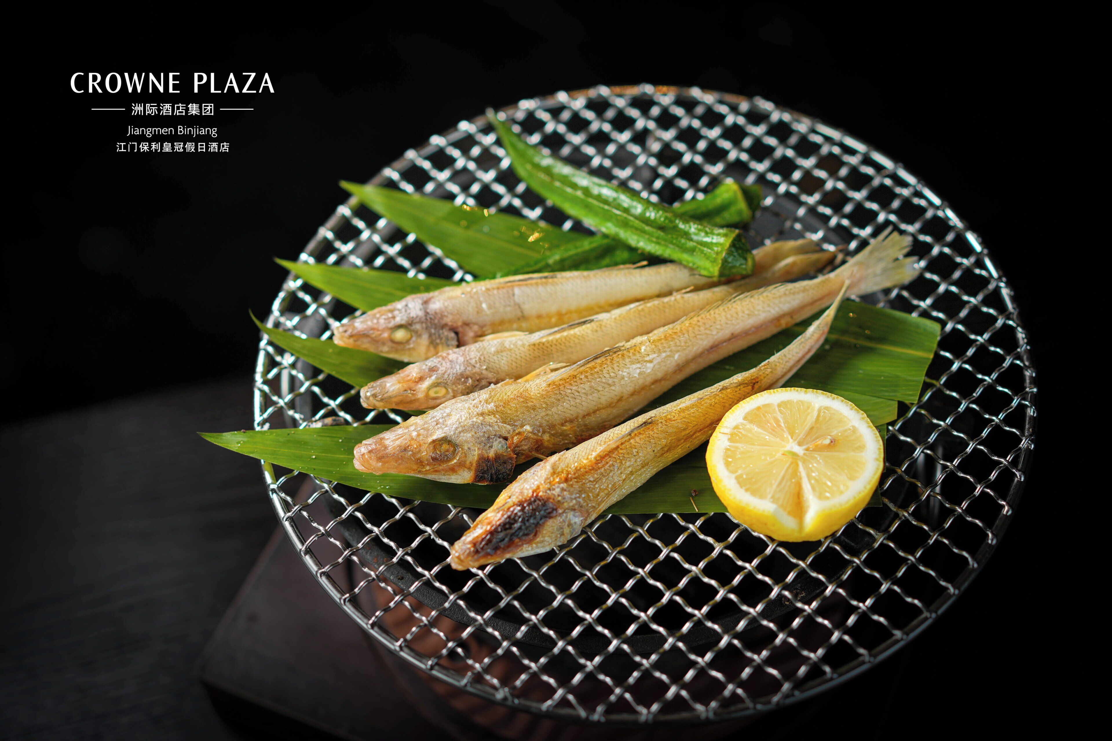 Grilled fish on a wire rack with a lemon slice and green leaves.