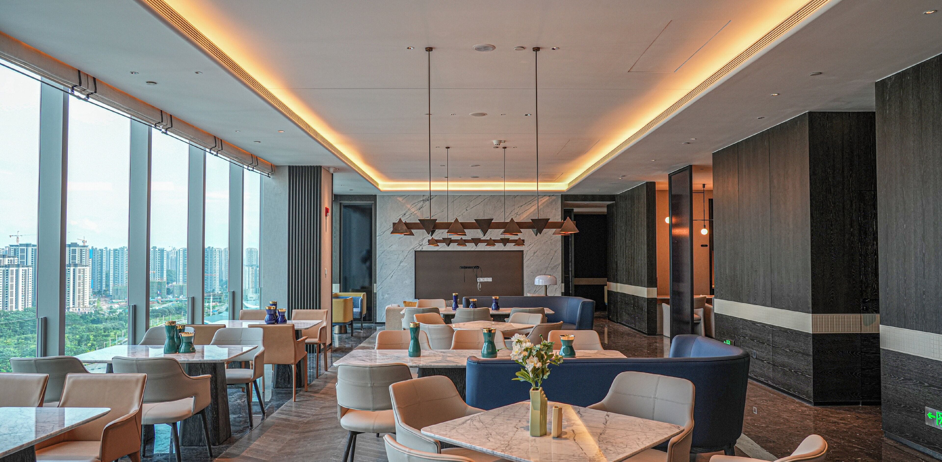 A modern hotel lobby with large windows, seating areas, and a view of the cityscape.