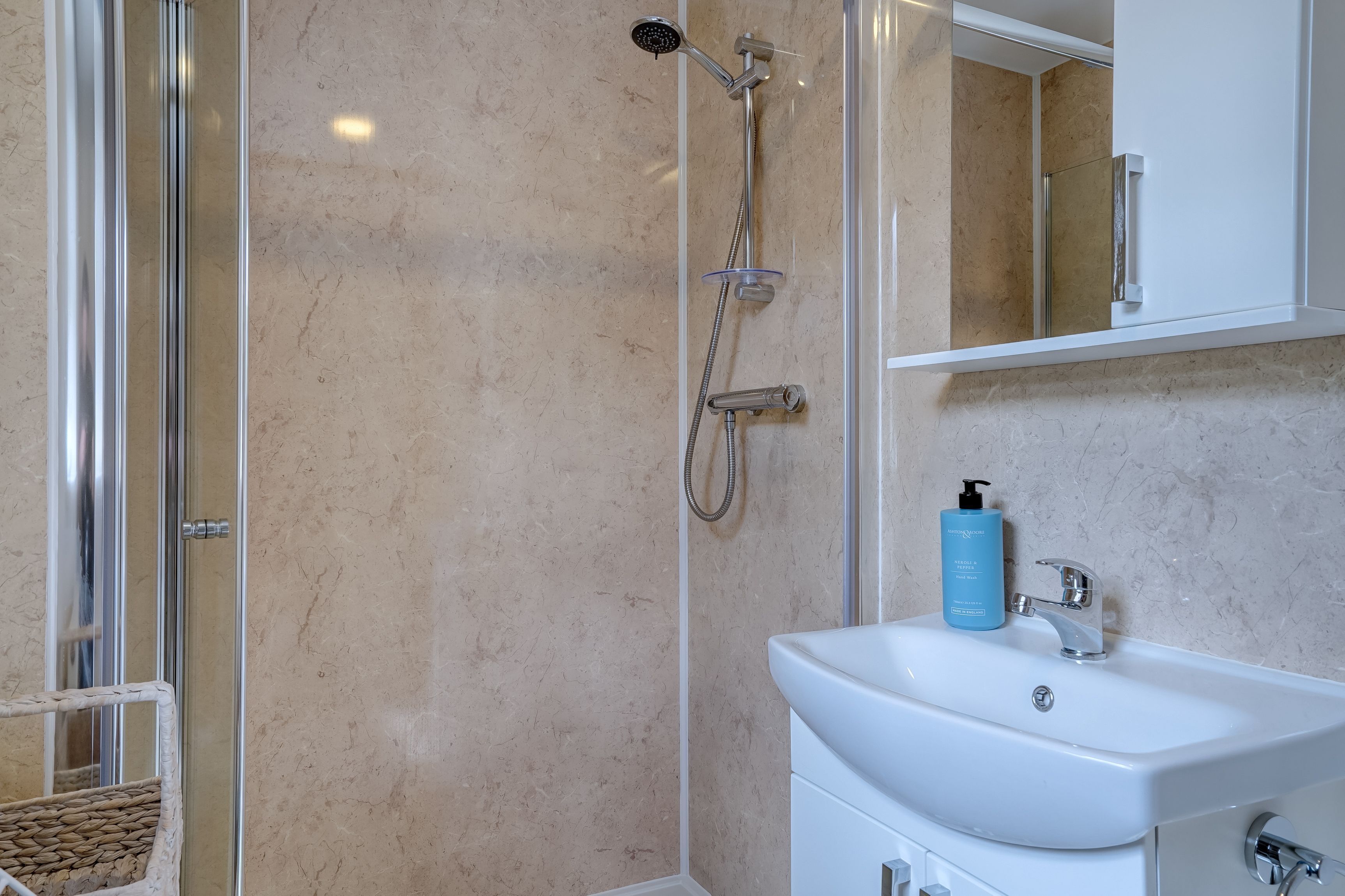 A bathroom with a glass shower enclosure, a white sink, and a mirror above it.