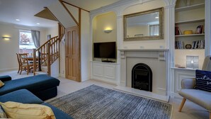 A living room with a fireplace, a television, and a staircase leading to another room. - The Old Village Shop | Spacious Dog Friendly Cottage Near the Beach (Winterton-on-Sea)