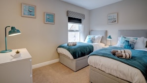 A bedroom with two beds, a window, and a desk with a lamp. - The Old Village Shop | Spacious Dog Friendly Cottage Near the Beach (Winterton-on-Sea)