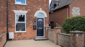 A brick house with a black front door, a small porch, and a mailbox. - The Old Village Shop | Spacious Dog Friendly Cottage Near the Beach (Winterton-on-Sea)